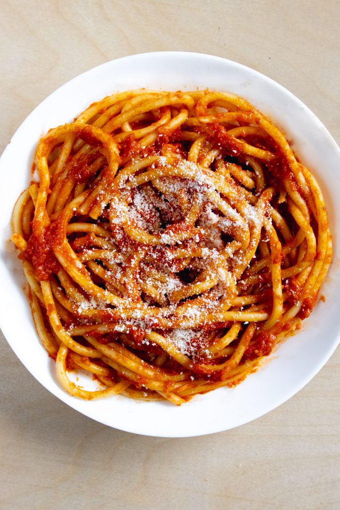 Bucatini pasta in bowl with tomato sauce and parmesan 