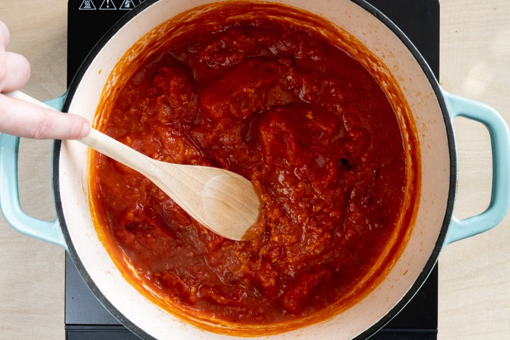 crushing tomatoes with wood spoon