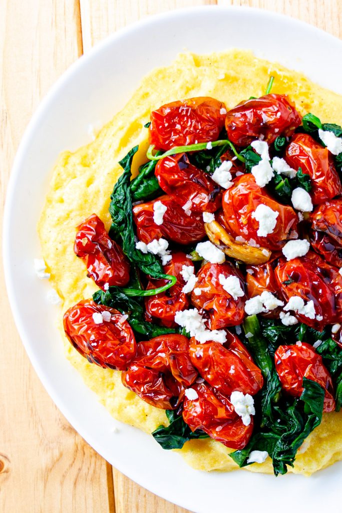 goat cheese polenta in a bowl topped with wilted spinach and tomato confit with balsamic glaze