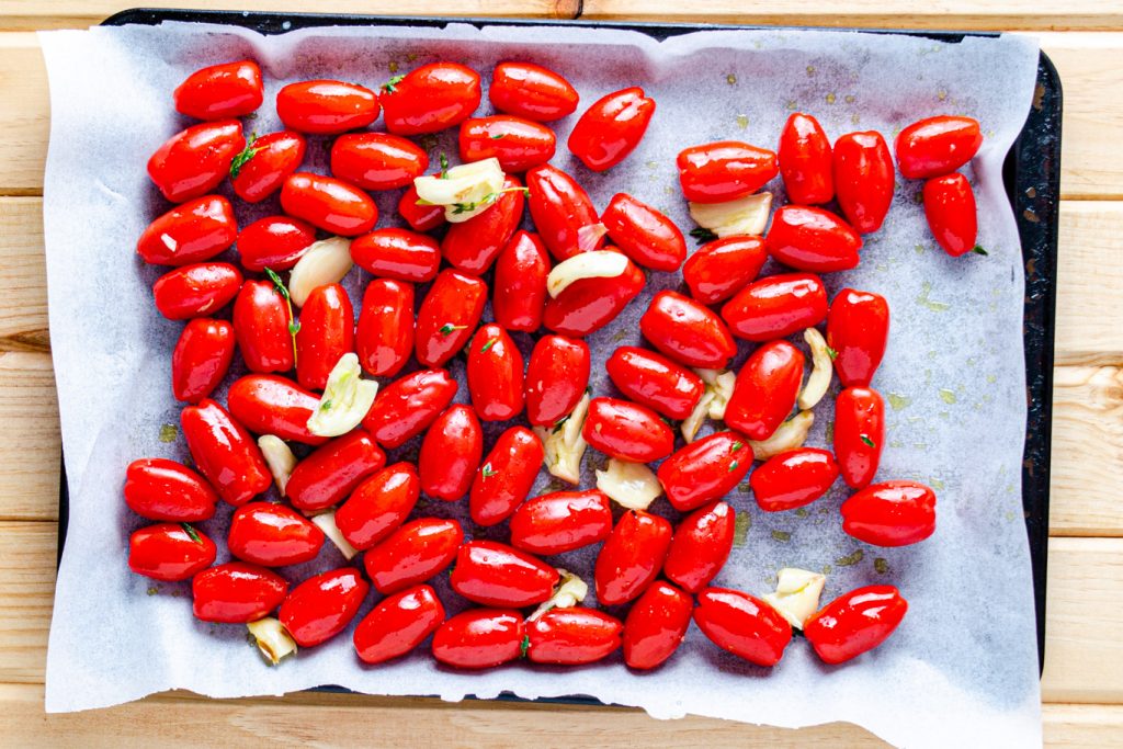 cherry tomatoes spread on sheet tray with garlic, thyme, and olive oil