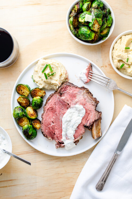 prime rib served bone-in with horseradish sauce and a side of roasted Brussels sprouts