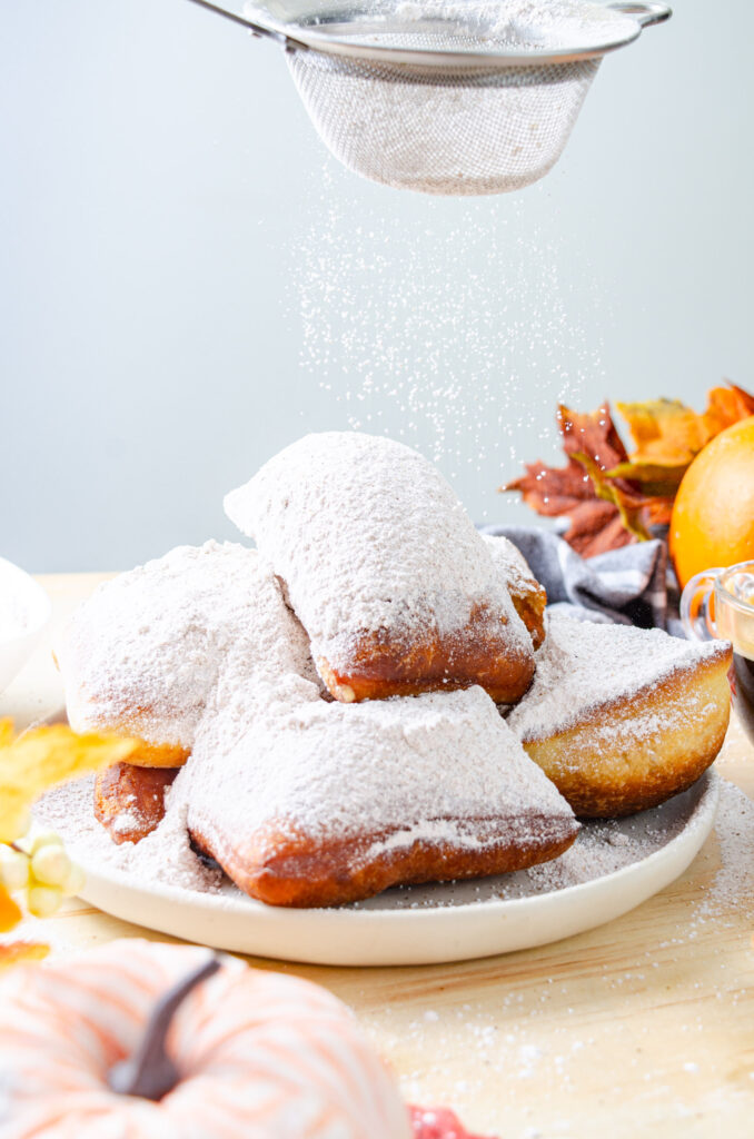 beignets being coated with powdered sugar