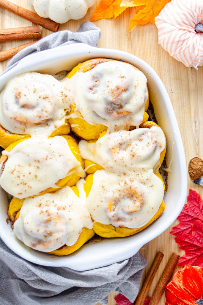 pumpkin cinnamon buns in baking dish with cinnamon roll icing