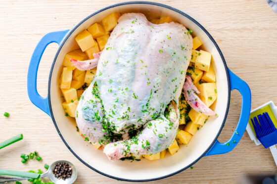 herb rubbed under chicken skin in Dutch oven sitting on top of rutabaga