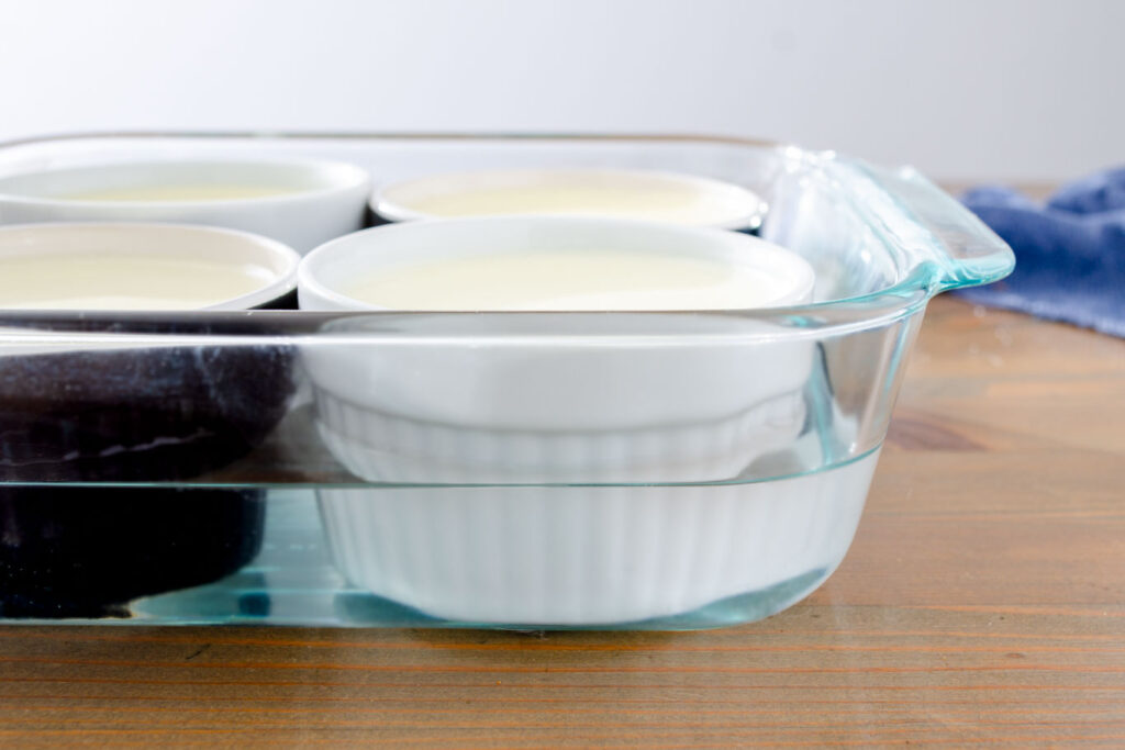 water bath with ramekins filled with vanilla custard